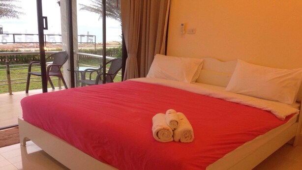A hotel room with a large bed, a balcony with chairs, and a view of the beach. - Saichol Resort (Chumphon)