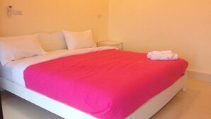 A bed with white bedding and a bright pink blanket, a white bedside table, and a white wall with a light switch. - Saichol Resort (Chumphon)