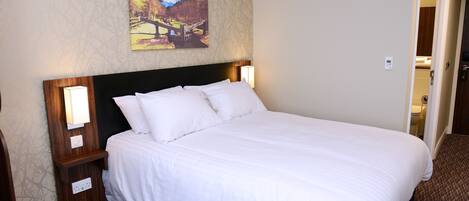 Una cama bien hecha con sábanas blancas, un cabecero de madera y dos lámparas de noche.