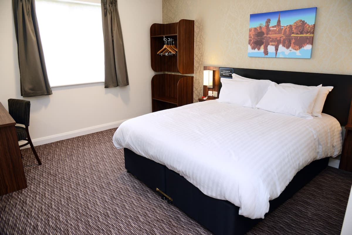 Una habitación de hotel con una cama grande, un armario de madera, un escritorio y una silla.