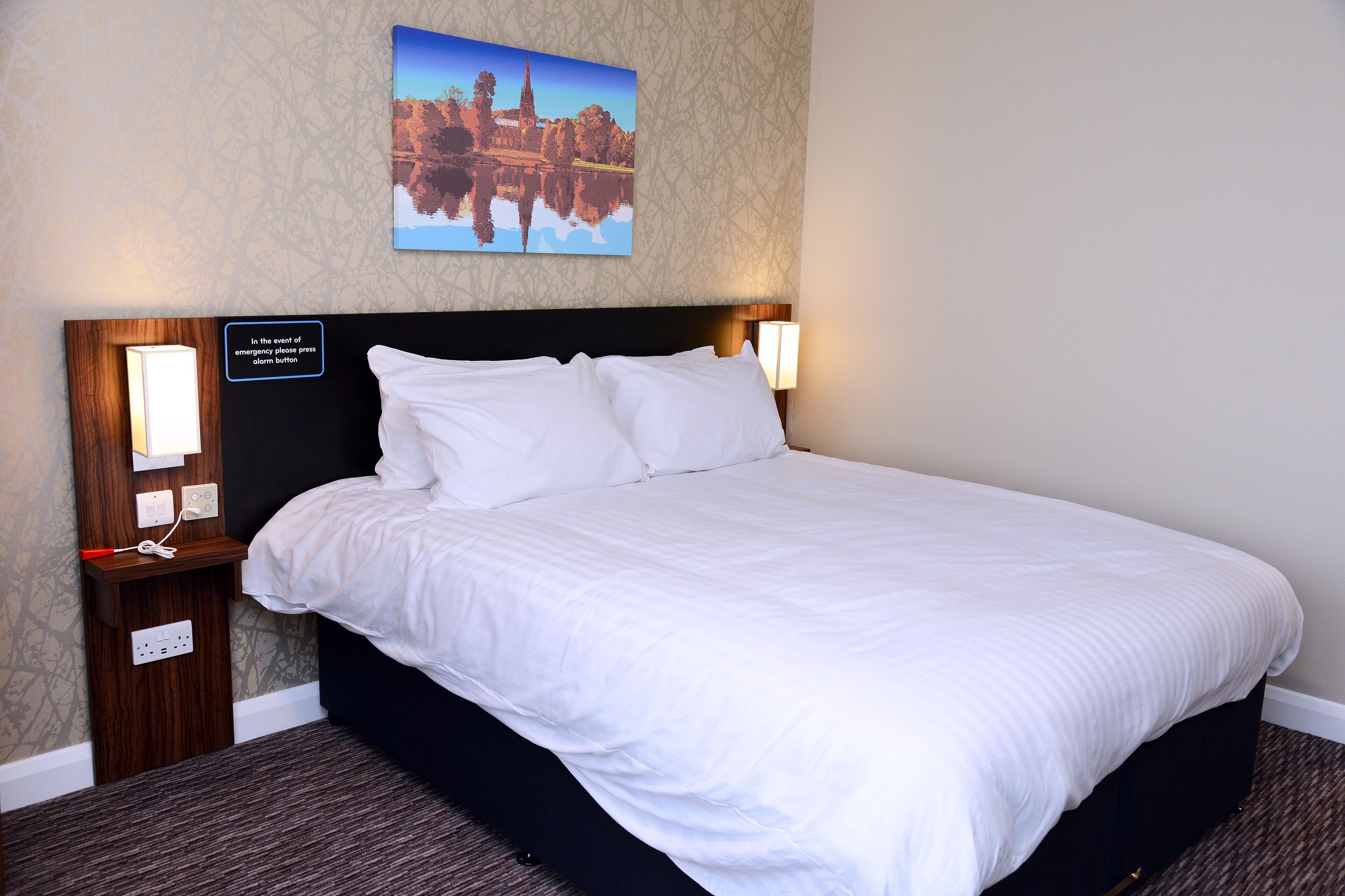 A neatly made bed with white linens, a dark headboard, and two bedside lamps.