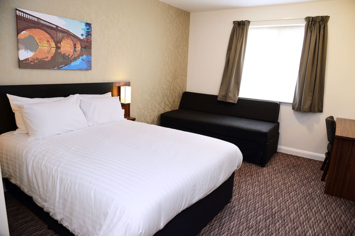 Habitación de hotel con una cama grande, un sofá, un escritorio y una ventana con cortinas.