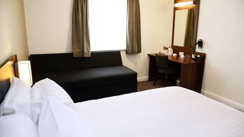 A hotel room with a bed, a desk, a chair, a mirror, and a window with curtains.