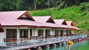 A row of wooden cabins with metal roofs, connected by a bridge over water. - Saichol Floating Resort (Ban Ta Khun)