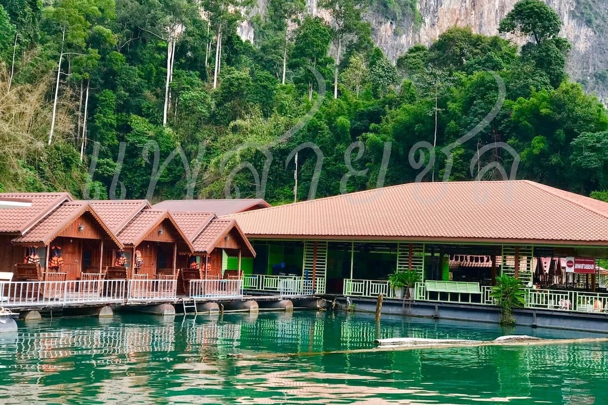 A hotel with multiple wooden buildings, a covered area, and a body of water in front.