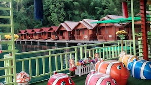 A row of wooden chalets with red roofs, a sign above them, and a body of water in the background. - Saichol Floating Resort (Ban Ta Khun)