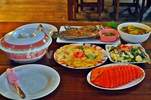 A dining table with various dishes including a whole fish, a bowl of soup, and a plate of sliced vegetables. - Saichol Floating Resort (Ban Ta Khun)