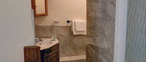 A bathroom with a sink, mirror, and shower area.