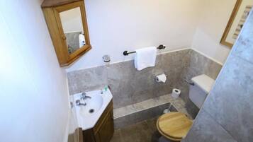 A bathroom with a wooden toilet, a sink, a mirror, and a towel rack.