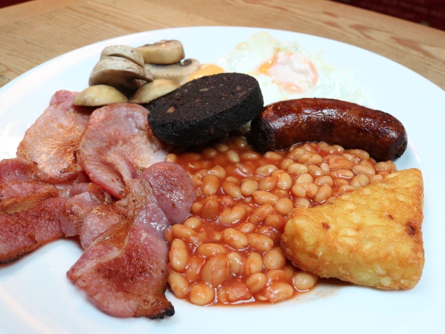 A plate of breakfast food including bacon, sausages, eggs, mushrooms, beans, and toast.