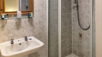 Un baño con lavamanos pedestal, cabina de ducha de vidrio y espejo con marco de madera.