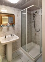 Un baño con lavamanos pedestal, cabina de ducha de vidrio y espejo con marco de madera.