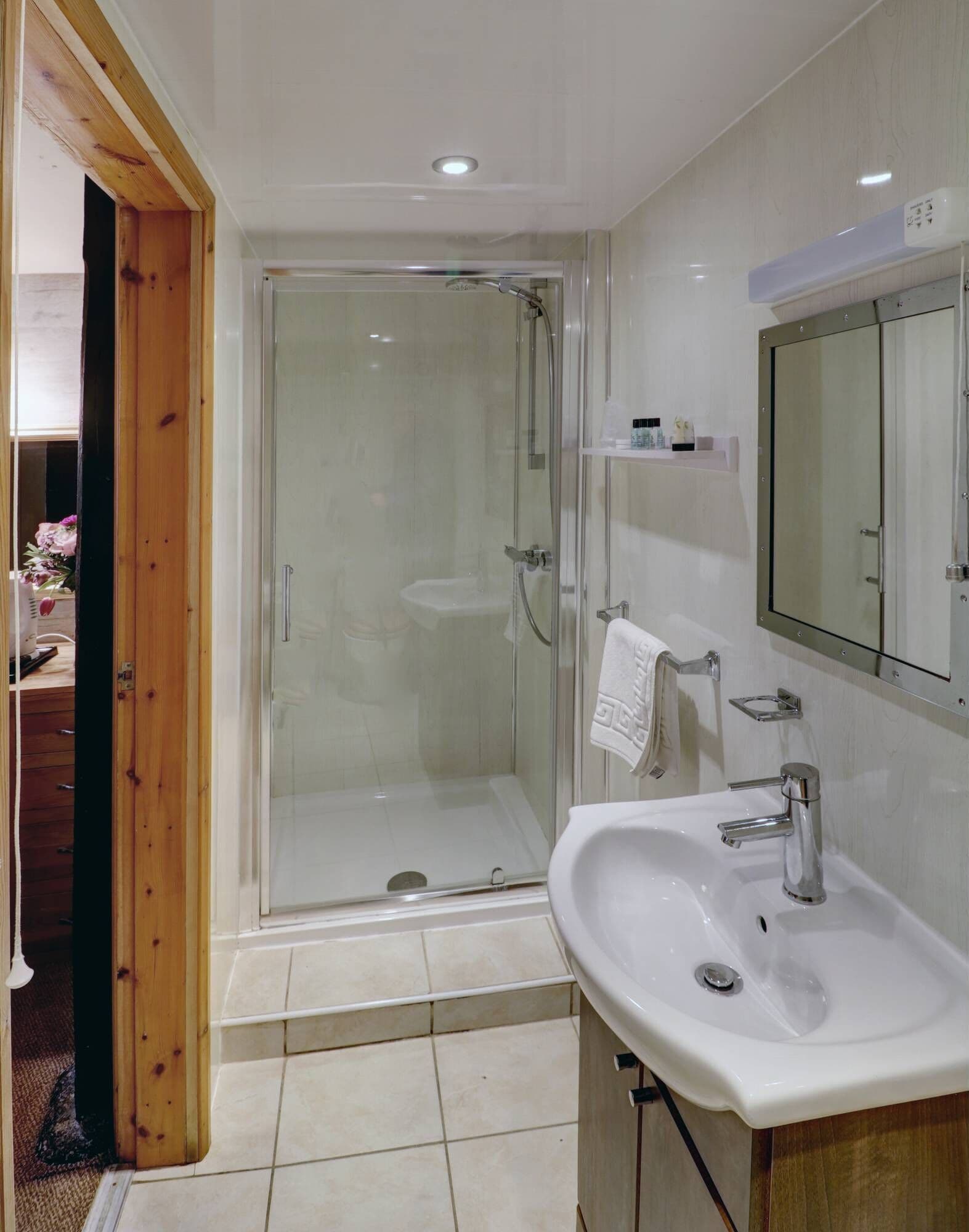 Un baño moderno con cabina de ducha de vidrio, un lavamanos blanco y un espejo sobre él.