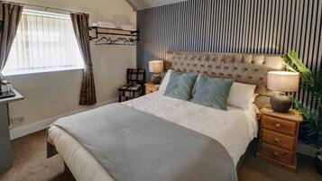 Quarto com cama grande, mesa de cabeceira com abajur, cadeira e janela com cortinas.