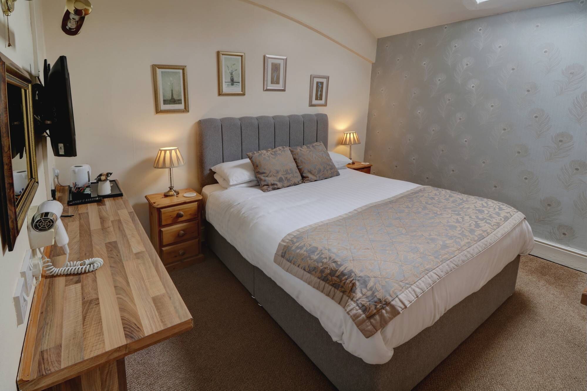 A bedroom with a large bed, a wooden desk, a hairdryer, and framed pictures on the wall.