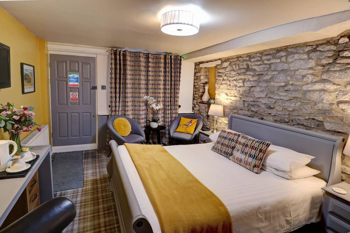 Una habitación de hotel con una cama, un escritorio con una silla, una lámpara y una pared de piedra.