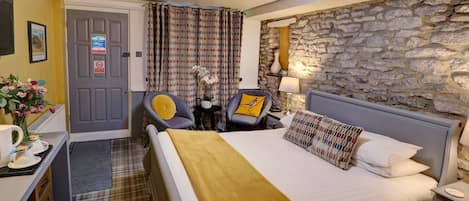 Una habitación de hotel con una cama, un escritorio con una silla, una lámpara y una pared de piedra.