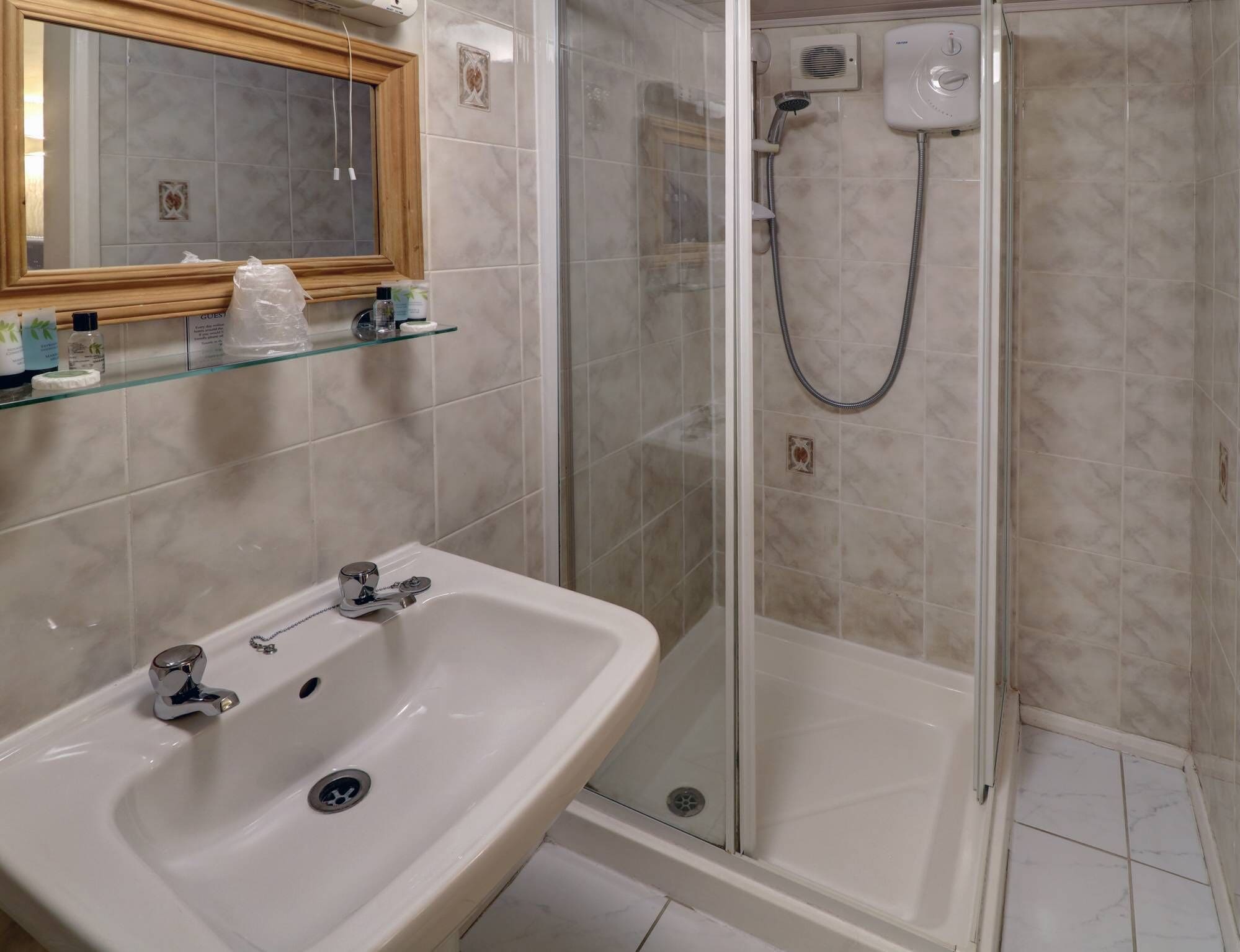 A bathroom with a sink, mirror, shower, and glass-enclosed shower stall.