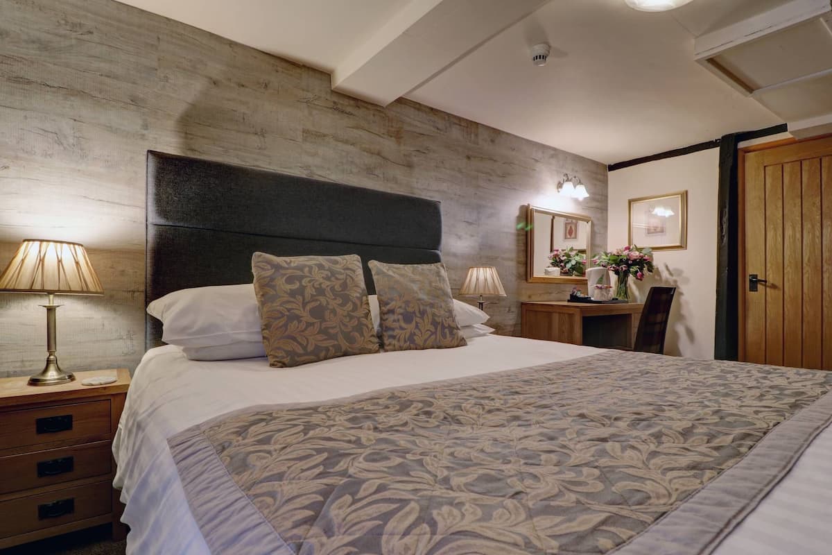 Una cama bien hecha con ropa de cama estampada, una lámpara de noche y una mesita de madera.