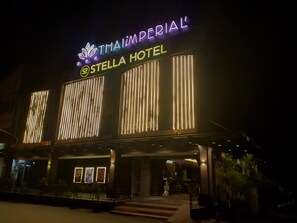 Exterior del Hotel Thai Imperial Stella con señalización iluminada y franjas verticales de luz en la fachada.
