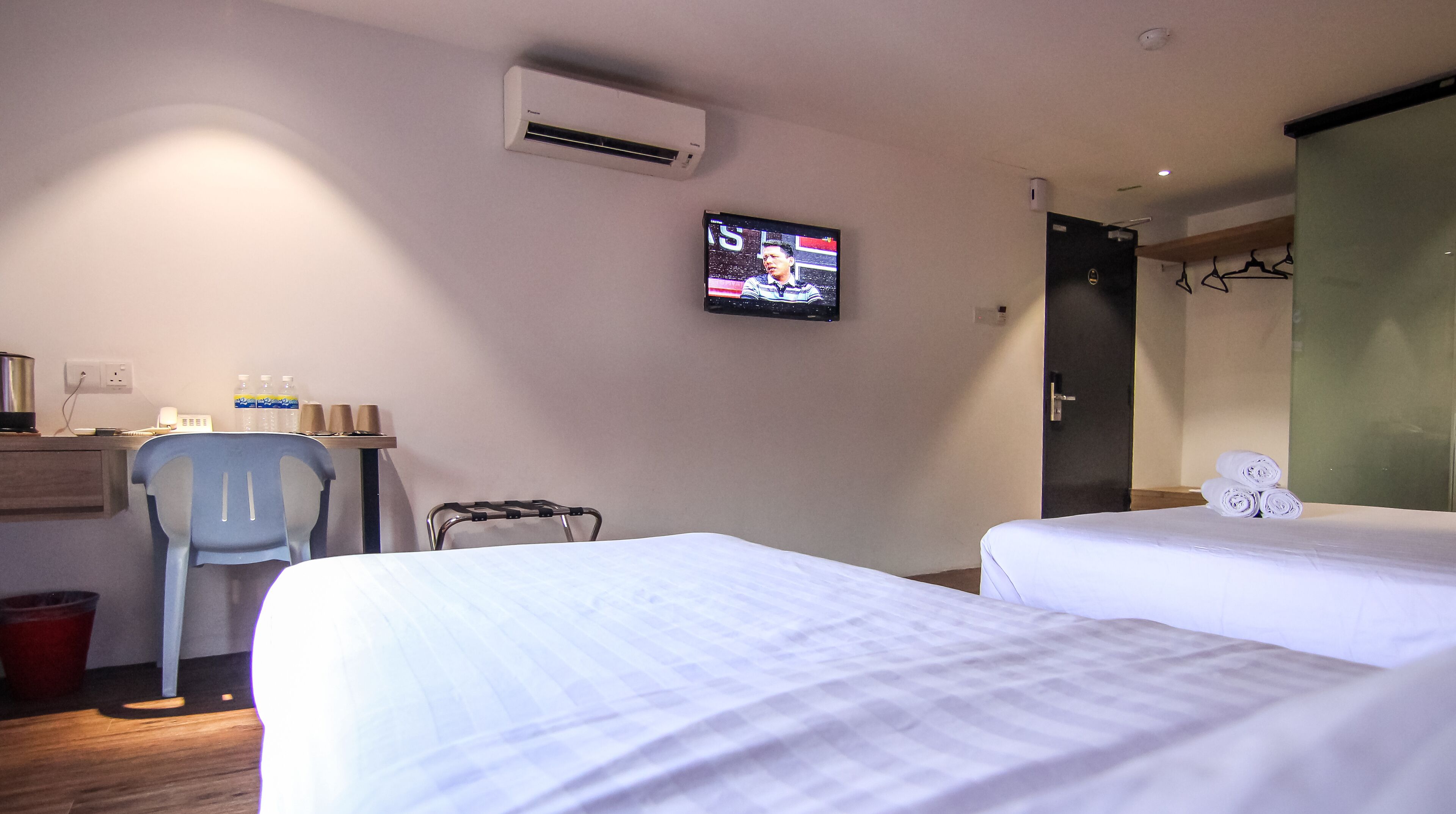 Ein Hotelzimmer mit zwei Betten, einem Schreibtisch mit Stuhl, einem Fernseher und einer Badezimmertür.