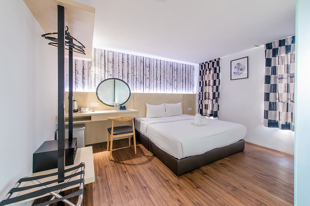 A modern hotel room with a bed, desk, chair, and a large mirror.