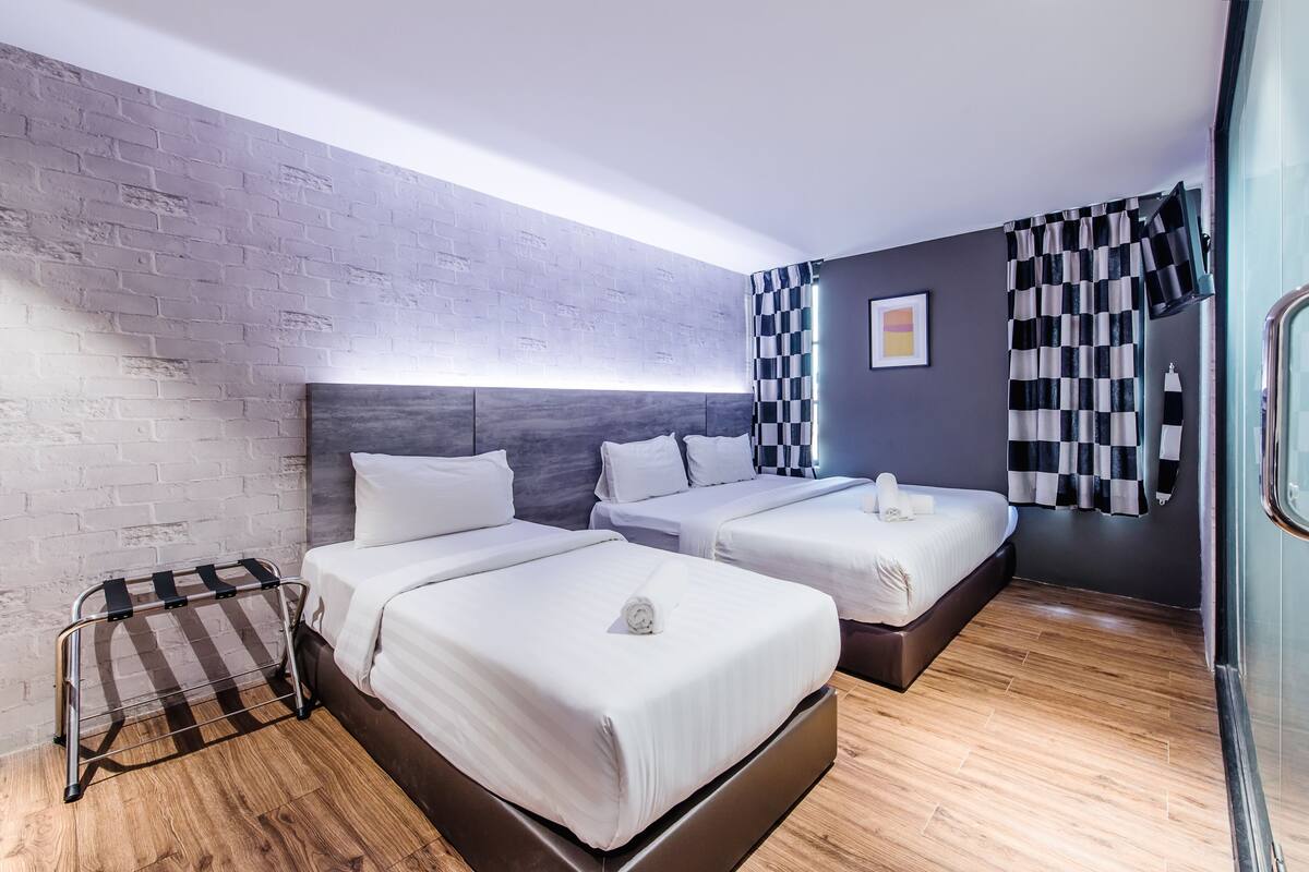 A modern hotel room with two beds, a metal rack, and a glass shower area.