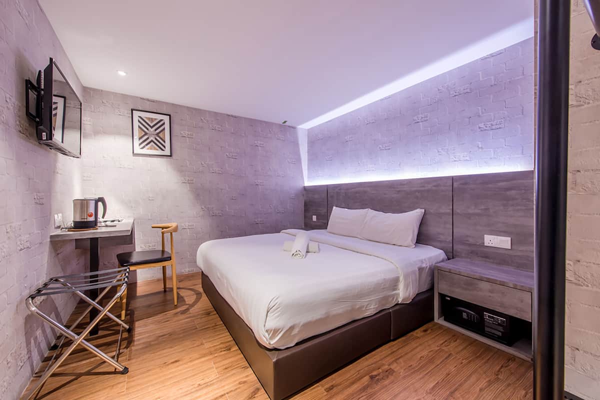 A modern bedroom with a large bed, a bedside table, a TV mounted on the wall, and a built-in bench under the bed.