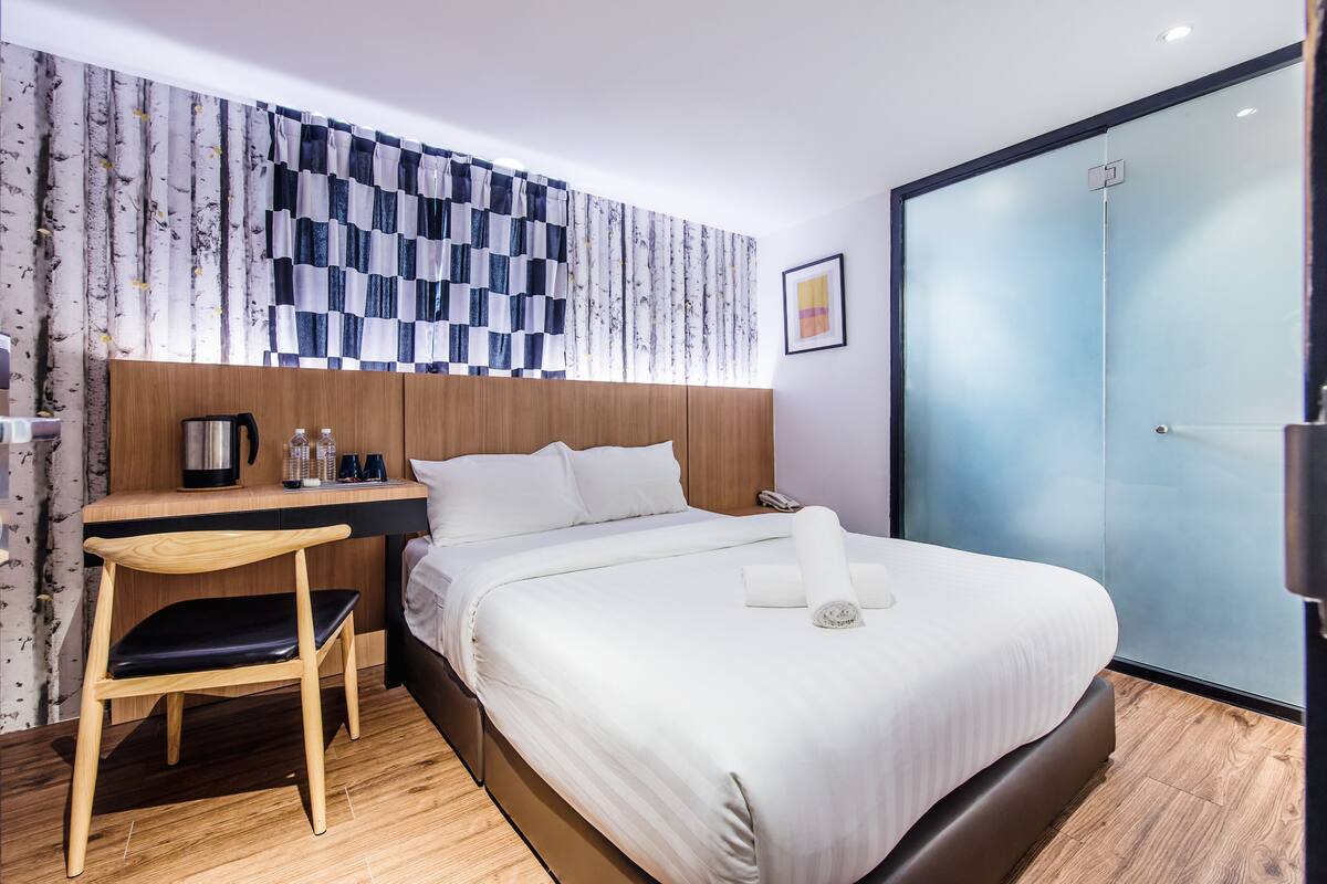 A modern hotel room with a bed, a desk, a chair, and a wardrobe.