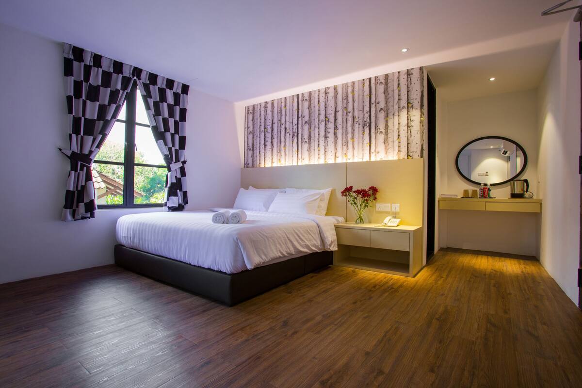A modern bedroom with a large bed, a bedside table with a lamp, a mirror, and a window with checkered curtains.