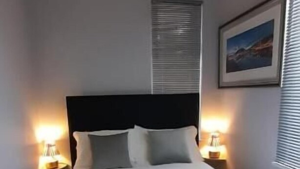 Una cama bien hecha con ropa blanca y toallas, cabecera oscura y lámparas de noche.