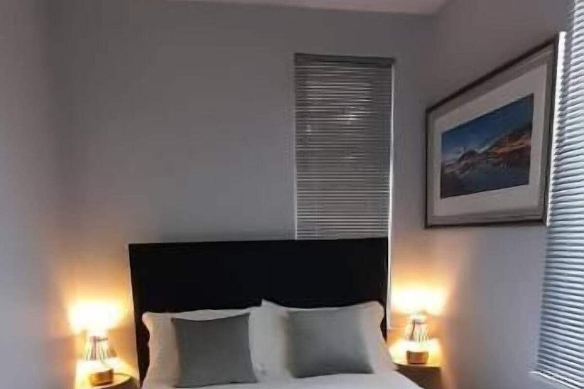A neatly made bed with white linens and towels, a dark headboard, and bedside lamps.