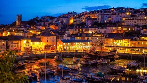 Un puerto con barcos amarrados, edificios con ventanas iluminadas y una torre destacada al fondo.