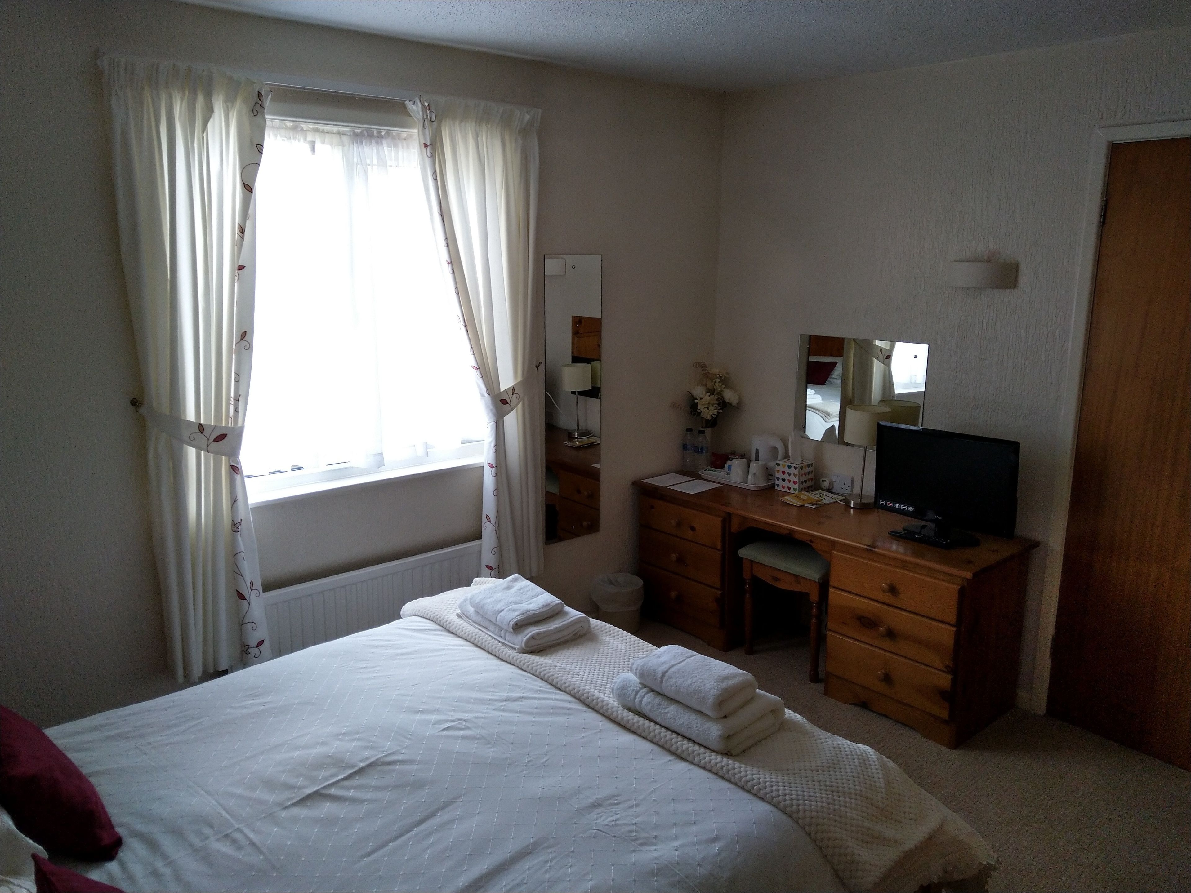 Een hotelkamer met een bed, een bureau, een stoel, een televisie en een raam met gordijnen.