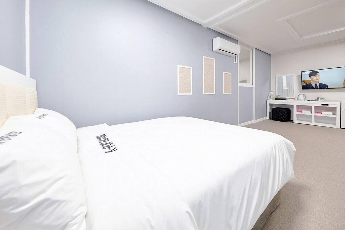 A hotel room with two beds, a flat-screen TV, a desk with a chair, and a small seating area.