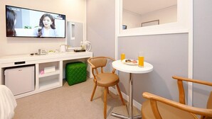 A modern hotel room with a flat-screen TV mounted on the wall, a small kitchenette, a round dining table with two chairs, and a green ottoman. - K-Pop Hotel (Gapyeong)