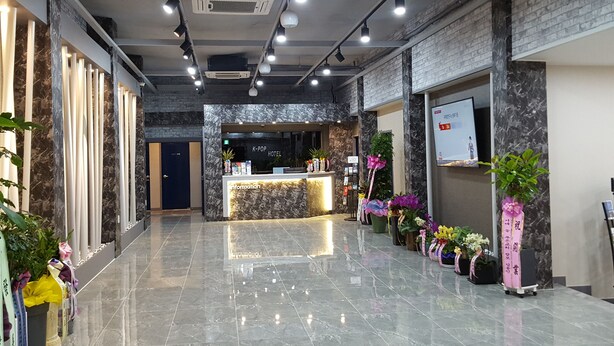 A hotel lobby with a marble reception desk, a K-pop themed sign, and various potted plants. - K-Pop Hotel (Gapyeong)