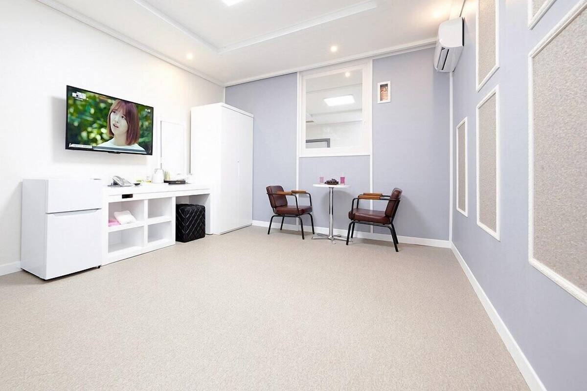 A modern room with a flat-screen TV, a white cabinet, two chairs, a small table, and a window.