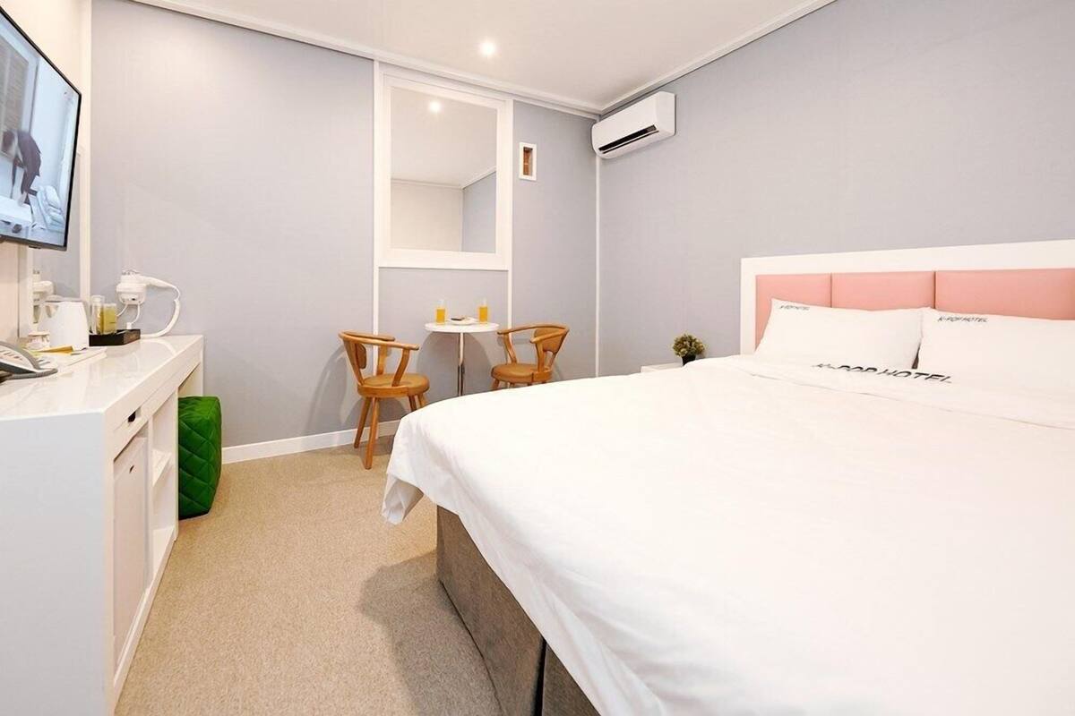 A hotel room with a bed, a desk, a chair, a small table, and a mirror.