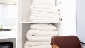 A neatly organized storage area with white bedding items, including pillows and a duvet, in a hotel room. - K-Pop Hotel (Gapyeong)