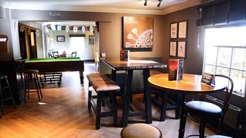 A bar area with a pool table, stools, and a wooden bar counter.