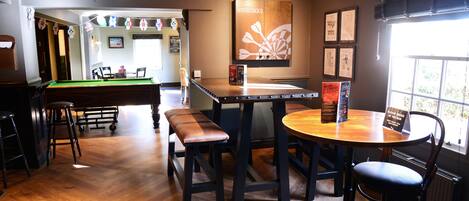 Un espace bar équipé d’une table de billard, de tabourets et d’un comptoir en bois.