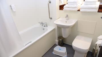 Et badeværelse med badekar, vask, toilet og en trinbræt.
