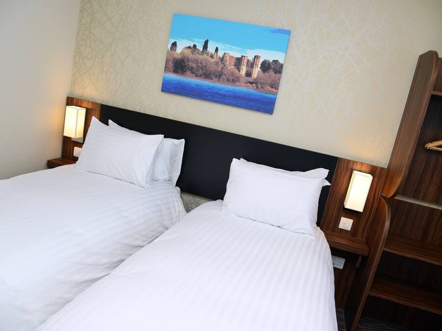 A hotel room with two beds, a wooden headboard, a wall-mounted painting, and bedside lamps.