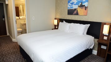 Habitación de hotel con una cama grande, un baño a la vista a través de una puerta abierta y un cuadro en la pared.