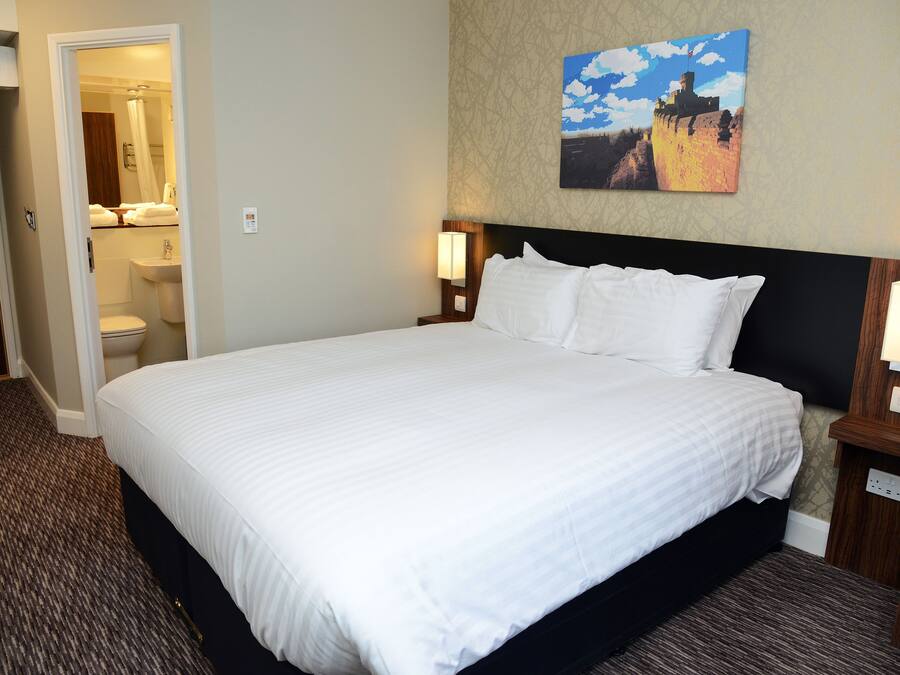 A hotel room with a large bed, a bathroom visible through an open door, and a painting on the wall.