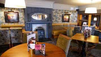 A hotel lobby with a fireplace, patterned wallpaper, and a round table with brochures.