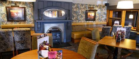 Een hotelhal met een open haard, behang met een patroon en een ronde tafel met brochures.