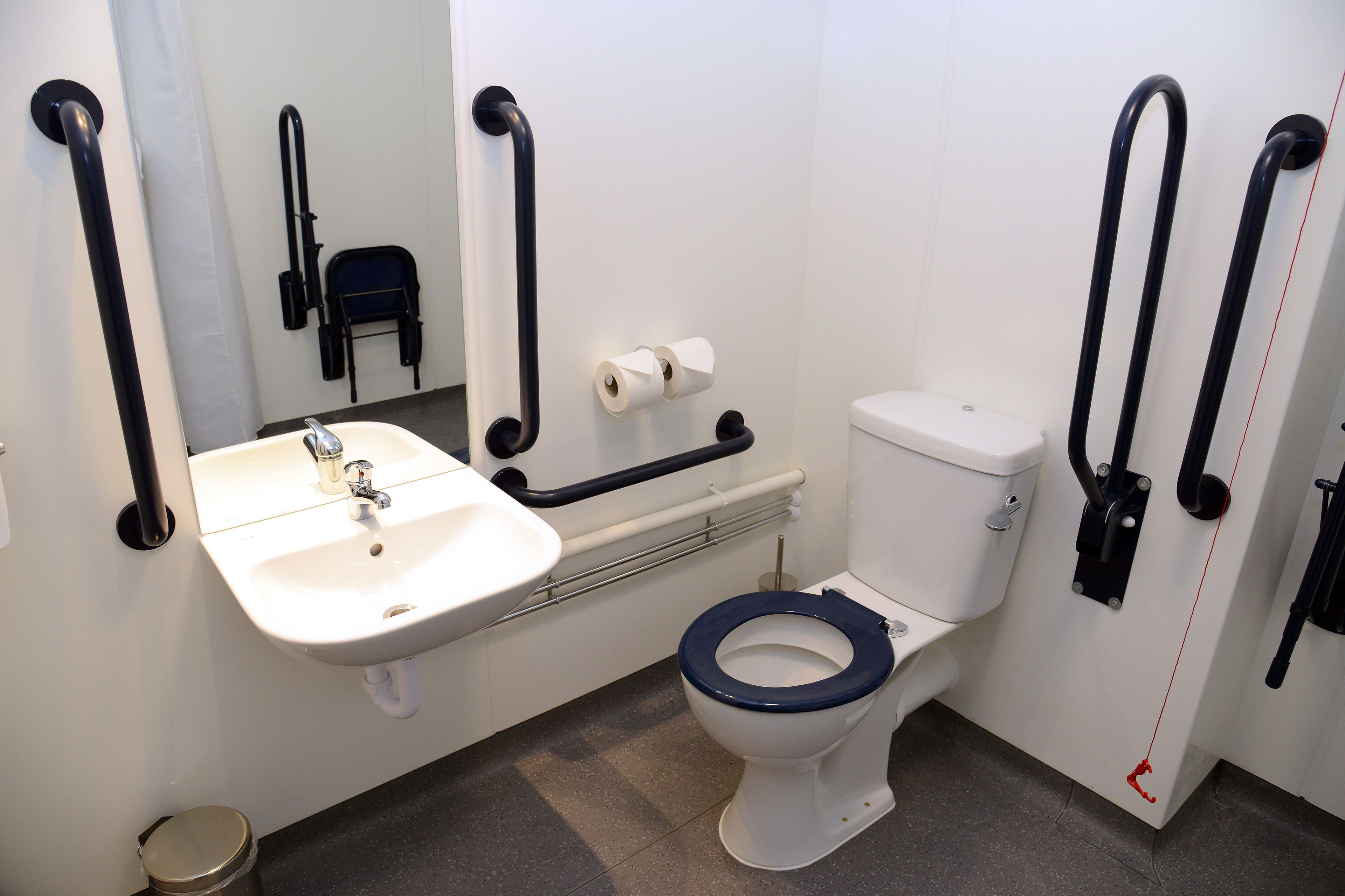Et badeværelse med en hvid vask, toilet og gelændere.
