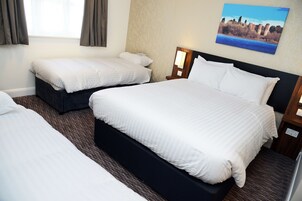 Habitación de hotel con dos camas individuales, una cama grande y una mesita de noche con lámpara.